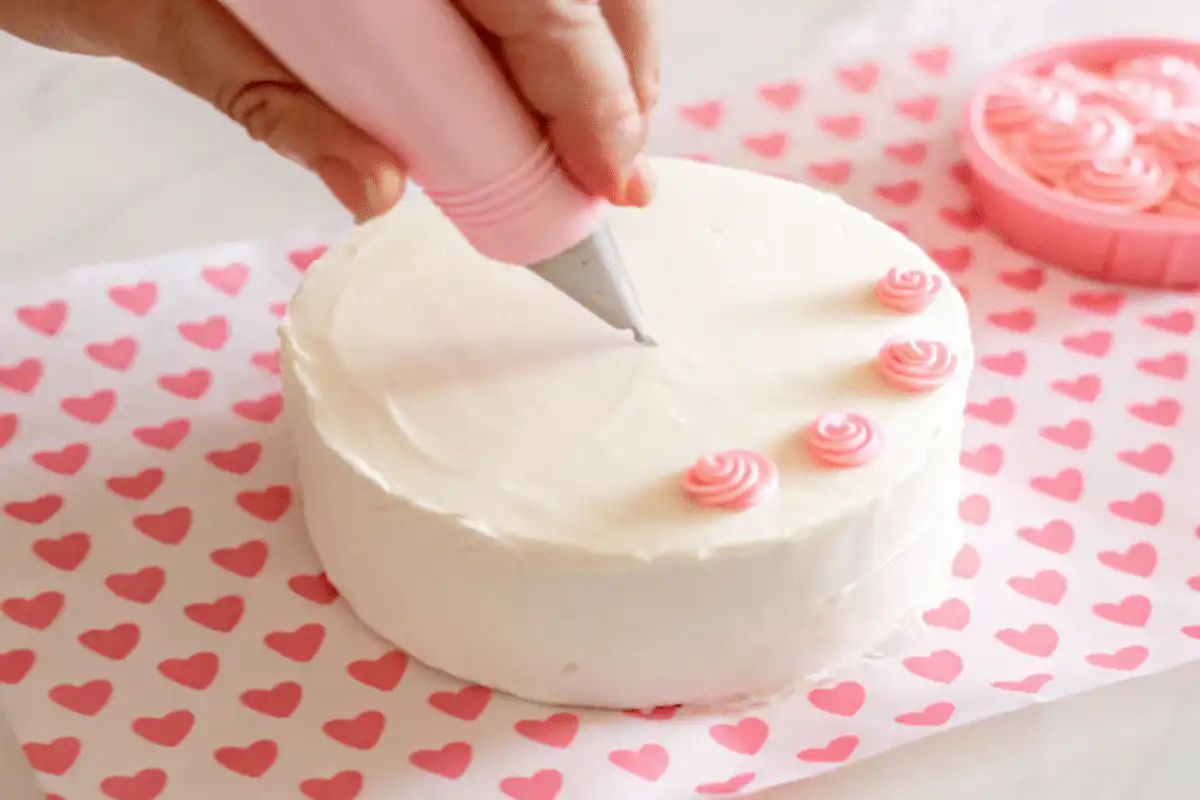 Piping pink buttercream rosettes onto mini bento cake