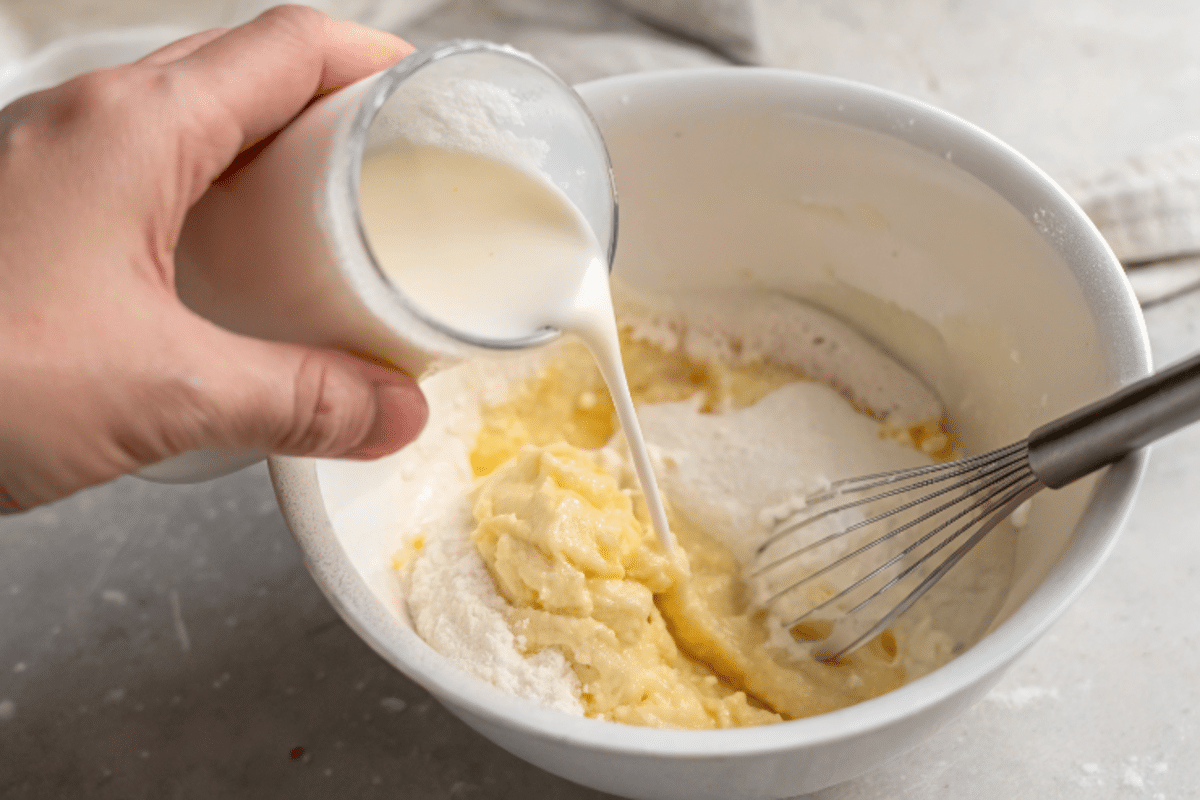 pouring-hot-milk-into-cake-batter Pouring hot milk into cake batter in white mixing bowl