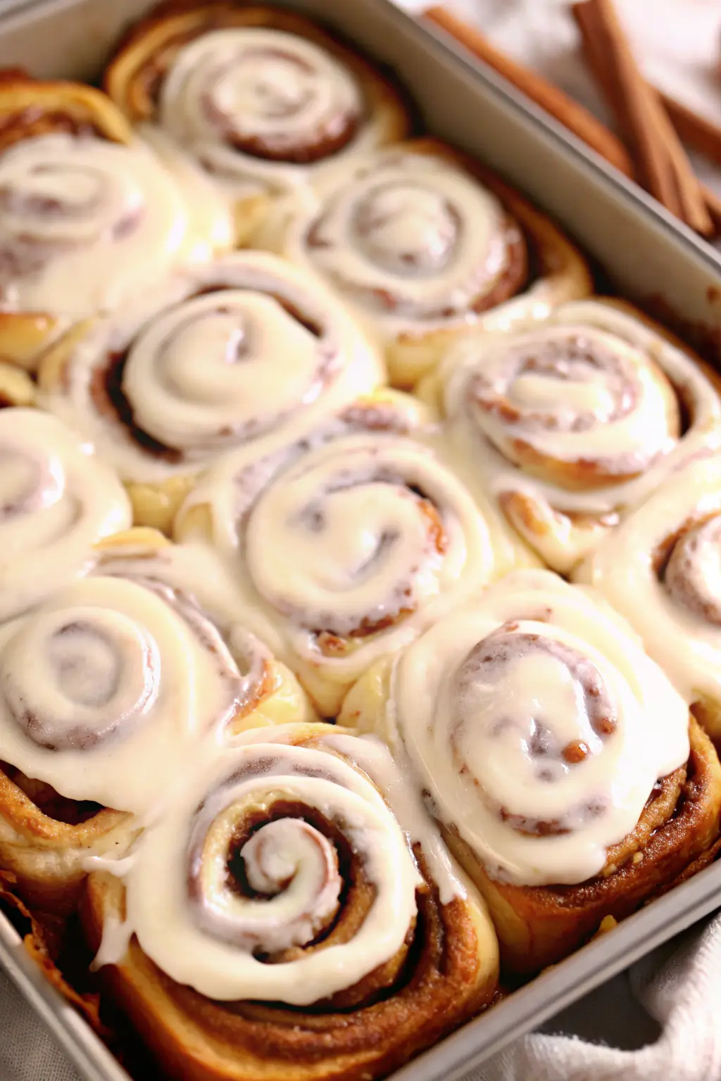 best-homemade-cinnamon-rolls-with-frosting Close-up of freshly baked cinnamon rolls topped with cream cheese frosting in a pan