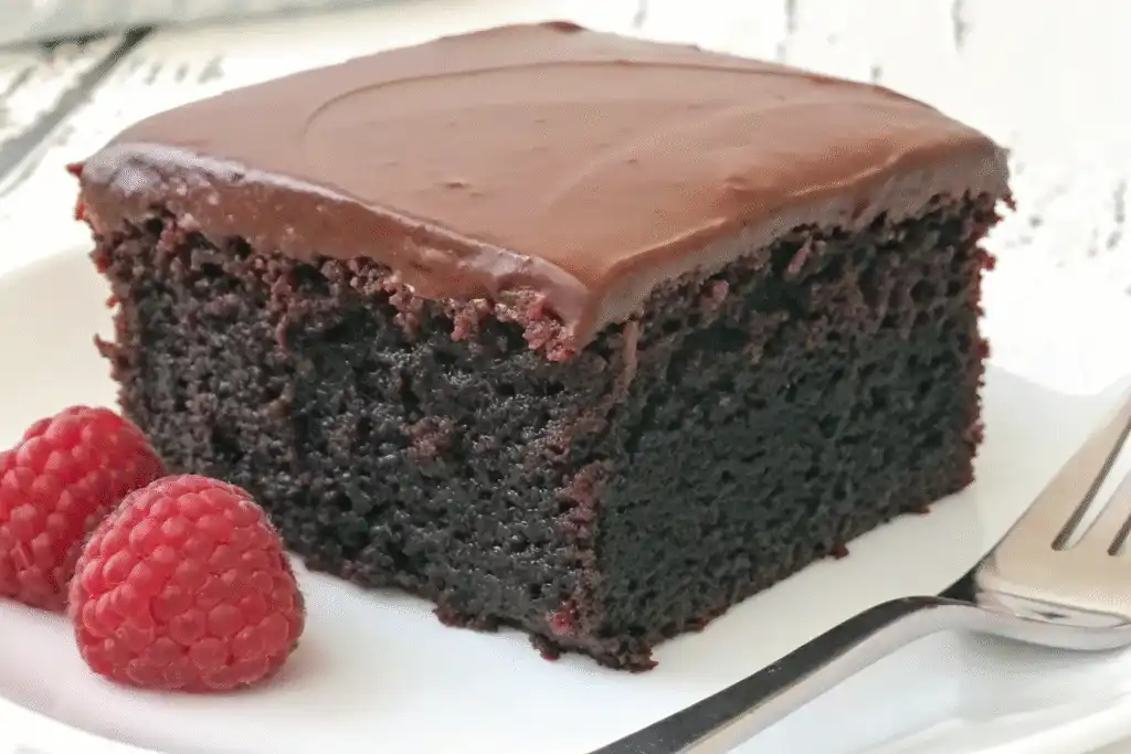 Moist homemade chocolate cake slice with rich frosting and fresh raspberries