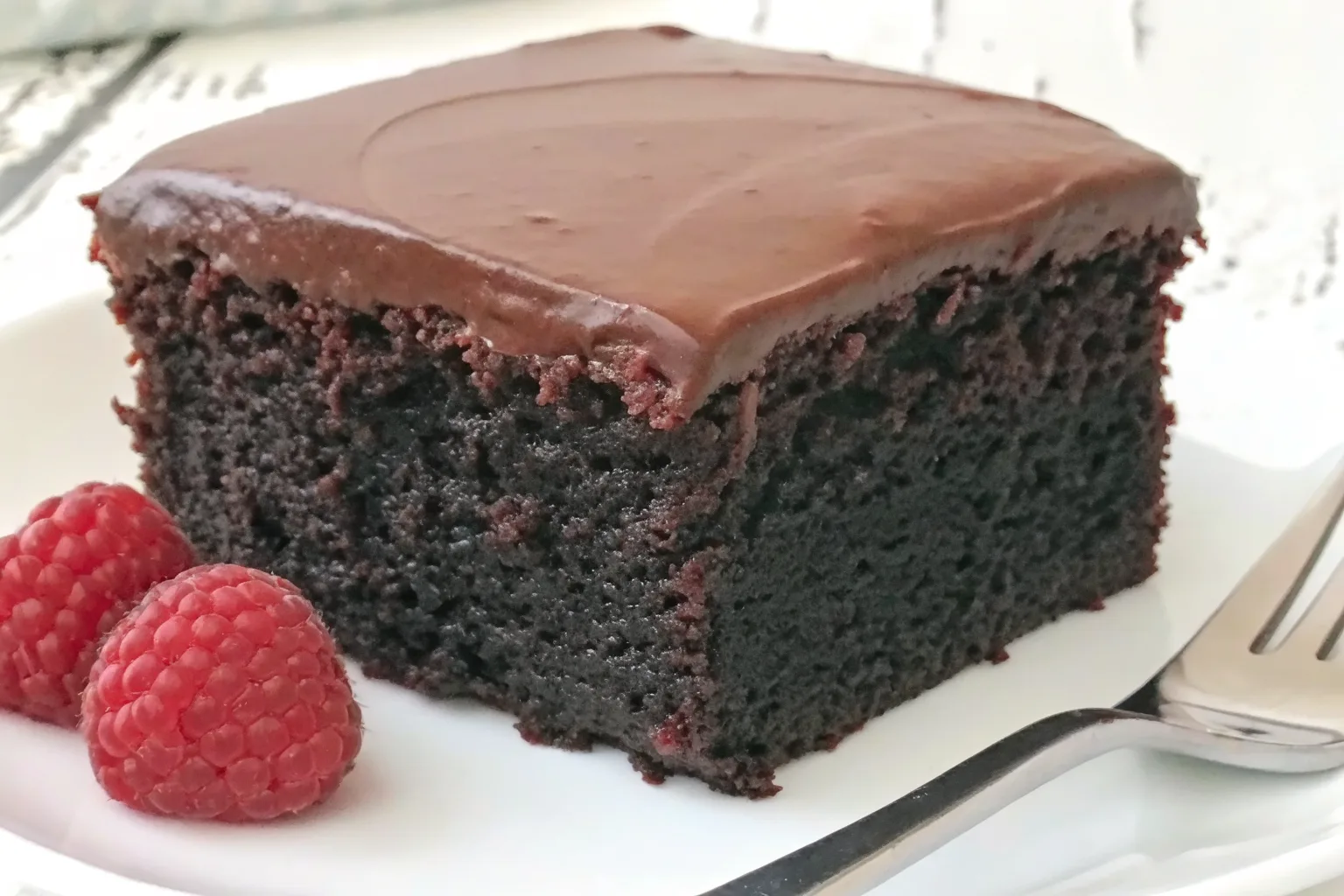 Moist homemade chocolate cake slice with rich frosting and fresh raspberries
