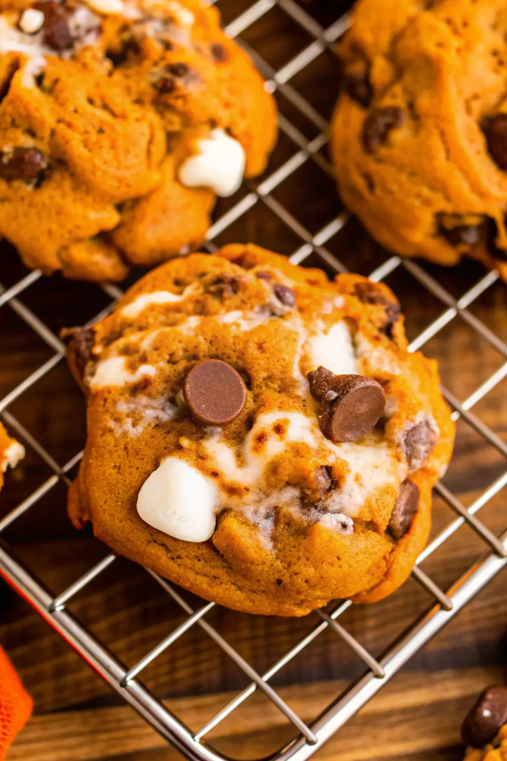 pumpkin-smores-cookies-soft-gooey Close-up of soft pumpkin s’mores cookies with gooey marshmallows and melted chocolate chips cooling on a wire rack.