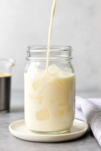 Pouring protein milk into glass with ice for protein coffee recipe