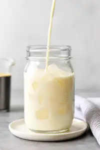 Pouring protein milk into glass with ice for protein coffee recipe