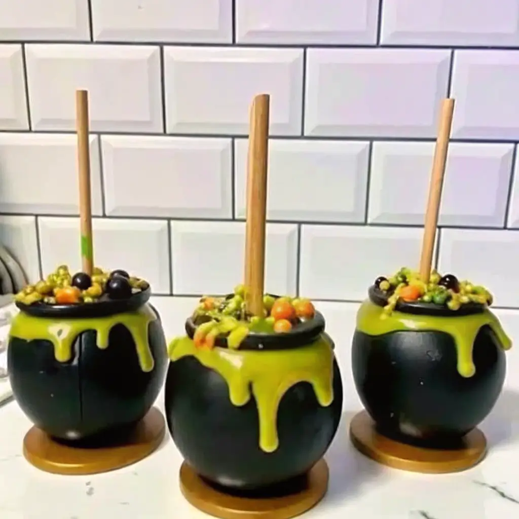 candy-apple-cauldron-halloween-treat Halloween candy apple cauldrons coated in black candy melts with green dripping icing and topped with candy decorations and wooden sticks.