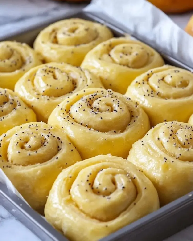 Freshly baked lemon rolls on a cooling rack with glaze drizzle