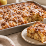 Glazed apple fritter cake in a rectangular pan with a square slice showing apple pieces and cinnamon swirls.